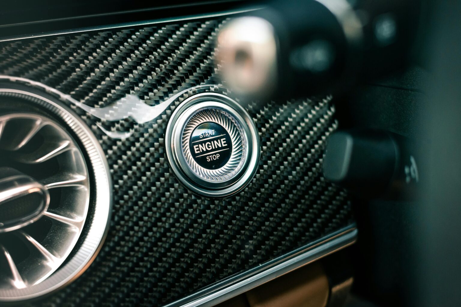 Detailed view of a car's engine start and stop button with carbon fiber finish.